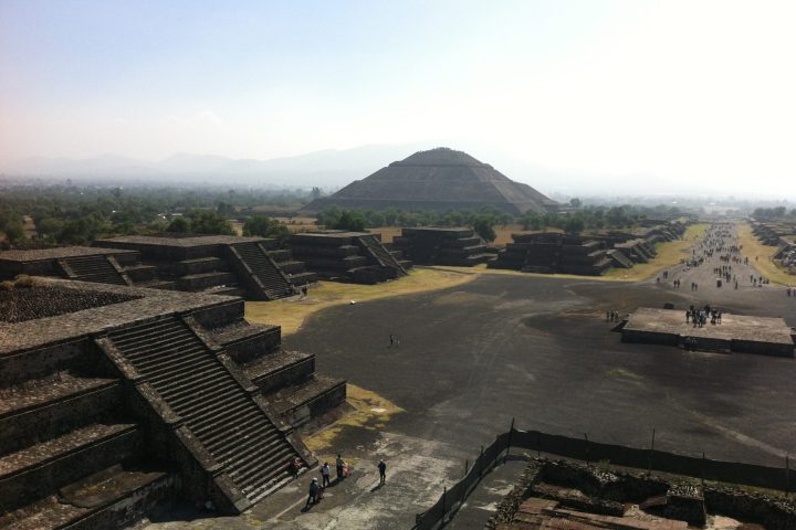 an empty park bench next to a body of water with Teotihuacan in the background